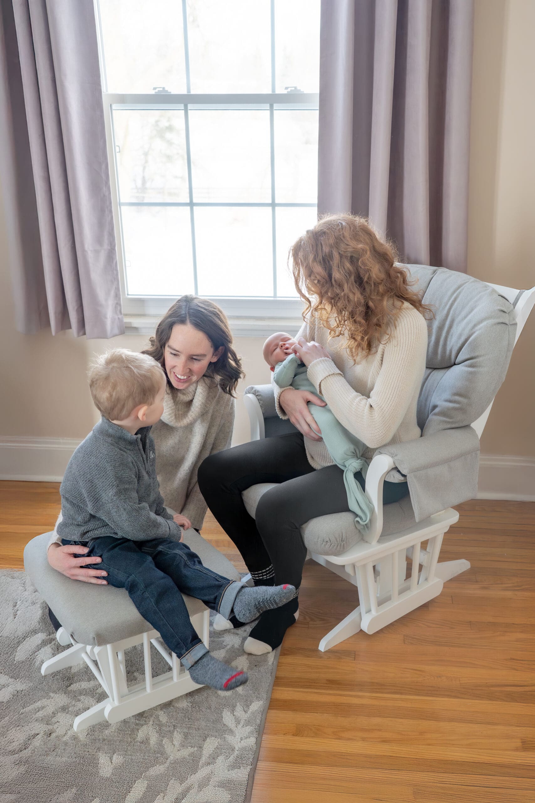 Lifestyle newborn photography session with two moms reading to toddler and holding baby in cozy nursery with natural light — photographed by Alliston and Barrie maternity, newborn, and family photographer.