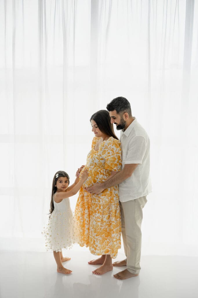 Expecting parents smiling at toddler during a soft, natural light maternity session — photographed by Alliston and Barrie maternity, newborn, and family photographer.