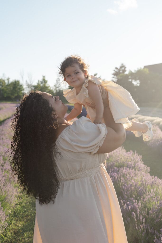 Mom holding toddler up high in lavender field during family photography session in Creemore