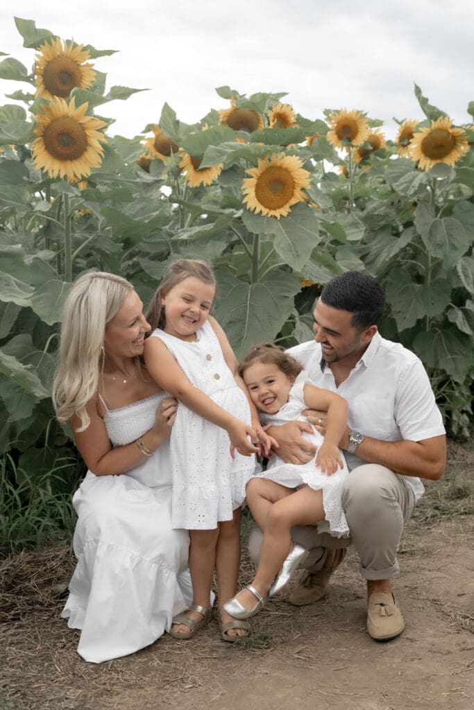Parent tickling daughters in sunflower field during family photography session in Innisfil
